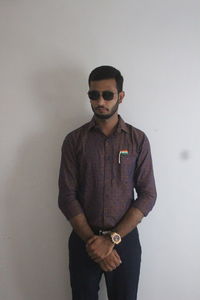 Portrait of young man wearing sunglasses standing against wall