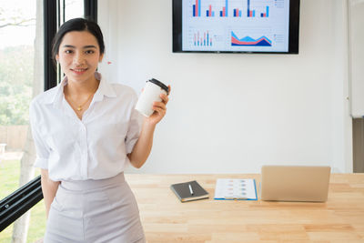 Portrait of businesswoman holding disposable cup while standing in office