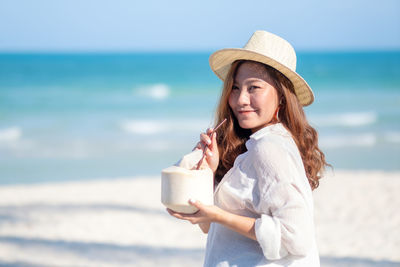 Smiling woman having drink at beach during sunny day