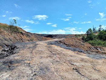 Dirt road passing through landscape against blue sky