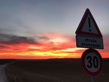 Road sign on field against sky during sunset