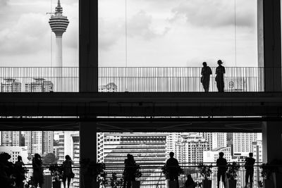 People walking on bridge against cloudy sky