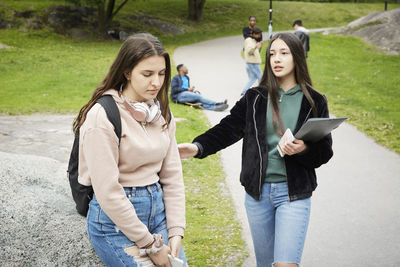 Teenage girl consoling sad female friends sitting on rock at park