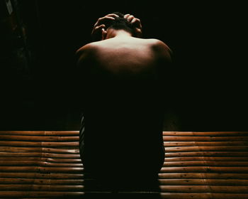 Rear view of shirtless depressed man sitting in darkroom