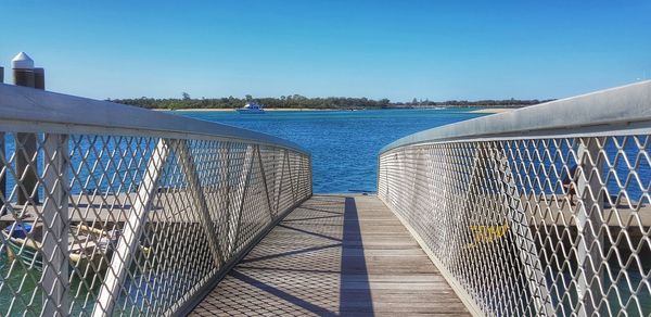 Footbridge over sea against clear blue sky