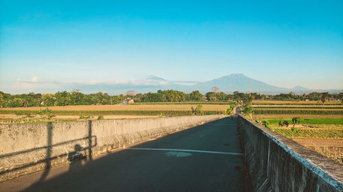 Road amidst field against clear blue sky