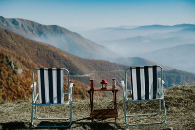 Empty chairs on road by mountains against sky