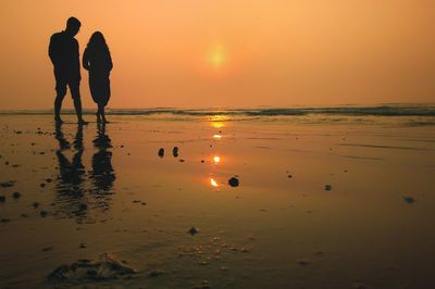 Silhouette people on beach against sky during sunset