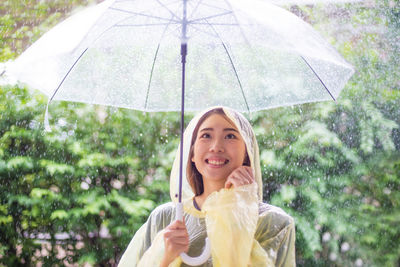 Smiling young woman holding umbrella during rainfall