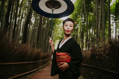 Young woman standing by tree in forest