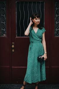 Portrait of smiling young woman standing against door