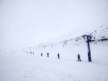 People skiing on snow covered field against sky