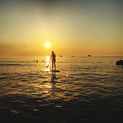 Silhouette people on sea against sky during sunset