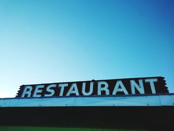 Low angle view of restaurant text against clear blue sky