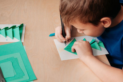 High angle view of boy holding paper on table