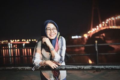 Smiling young woman sitting on illuminated city at night