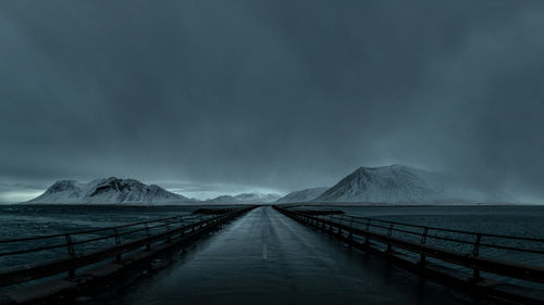 Empty road amidst landscape leading snowcapped mountains against sky