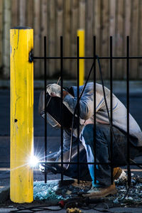 Welder holding mask while welding fence