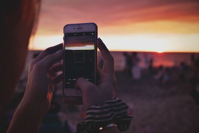 Cropped hand photographing sunset