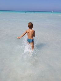 Rear view of shirtless boy wading in sea