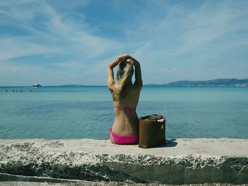 Rear view of woman sitting on retaining wall by sea against sky