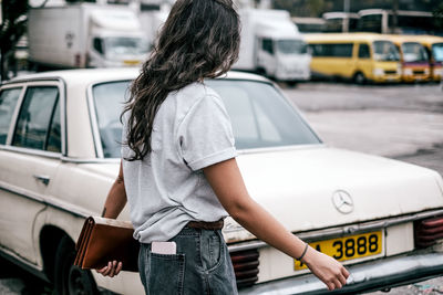 Rear view of woman standing against car