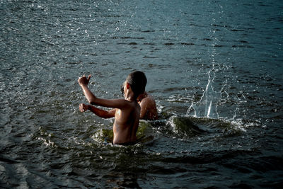 Rear view of shirtless man splashing water in sea