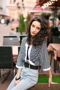 Woman on the street at the cafe . dark curly hair brown eyes . posing for the camera. 