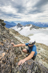 Climber wearing helmet scrambles up toward the summit of a mountain.