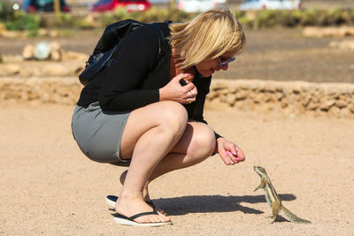 Full length side view of woman looking at squirrel while crouching on land