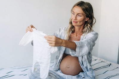 A young beautiful pregnant mother holds in her hand and looks at an infant bodysuit.