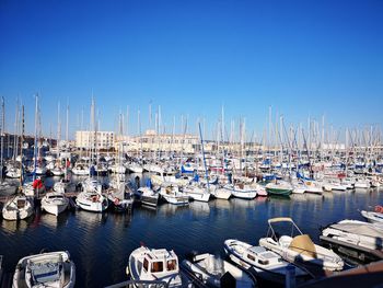 Boats moored at harbor against clear blue sky