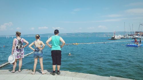 Rear view of people standing by sea against sky