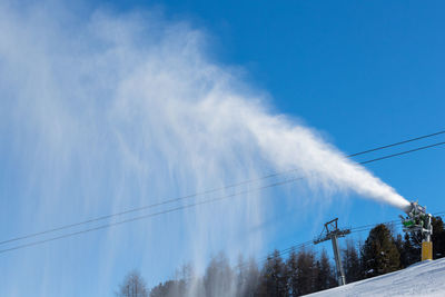 Low angle view of snowblower blowing snow against clear blue sky