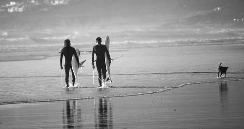 Rear view of people with surfboards walking on beach