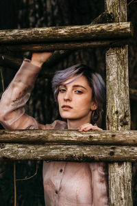 Portrait of young woman holding wooden fence