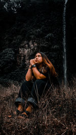 Beautiful young woman sitting on land against trees