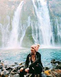 Young woman sitting on rock by waterfall