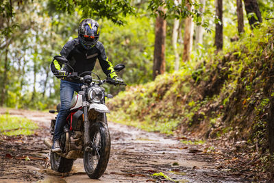 Man riding his scrambler type motorcycle through forrest