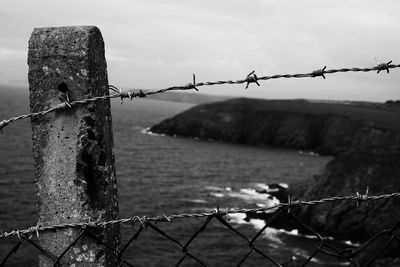 Close-up of barbed wire fence against sea