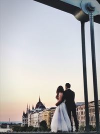 Rear view of just married couple standing against sky during sunset