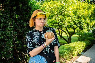 Beautiful young woman standing by plants against trees