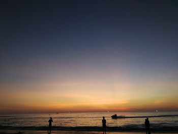 Silhouette people on beach against sky during sunset