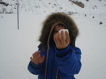 Portrait of boy holding ice on snow covered field