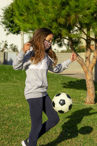 Cute girl wearing mask playing soccer at park