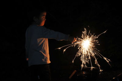 Boy holding lit sparkler at night