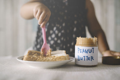 Midsection of girl spreading peanut butter on bread in plate at home