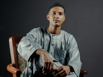 Portrait of young man sitting against black background