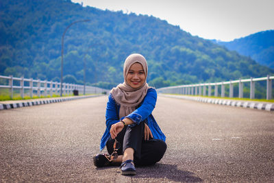 Portrait of smiling young woman on road against mountains