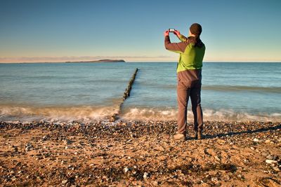 Rear view of man standing at beach against sky